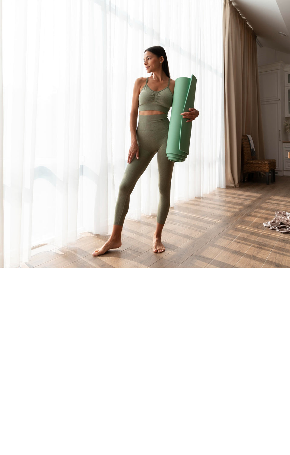  A woman in a green sports bra and leggings stands in front of a yoga mat, showcasing her readiness for yoga practice.